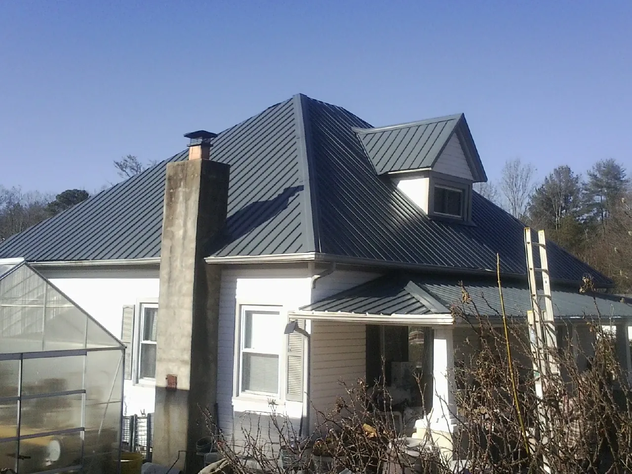 Dark blue standing seam metal roof on a white farmhouse with dormer — Slate & Tile Roof Repair by Roofing Brothers in Southfield