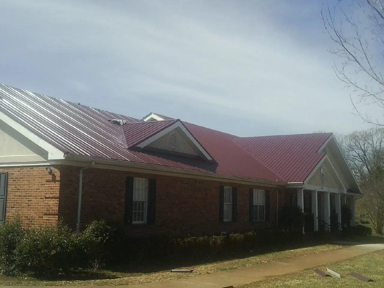 Red metal roof with gabled entries on a long brick building, from a Hail Damage Roof Repair job in Southfield
