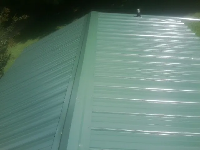 New green metal panels meeting at the ridge of a roof — Flat Roof Repair work by our crew in Southfield