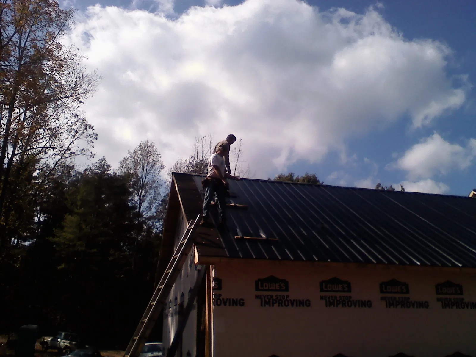 Roofer fastening dark metal panels high against a cloudy sky, from a Roof Inspection job in Southfield