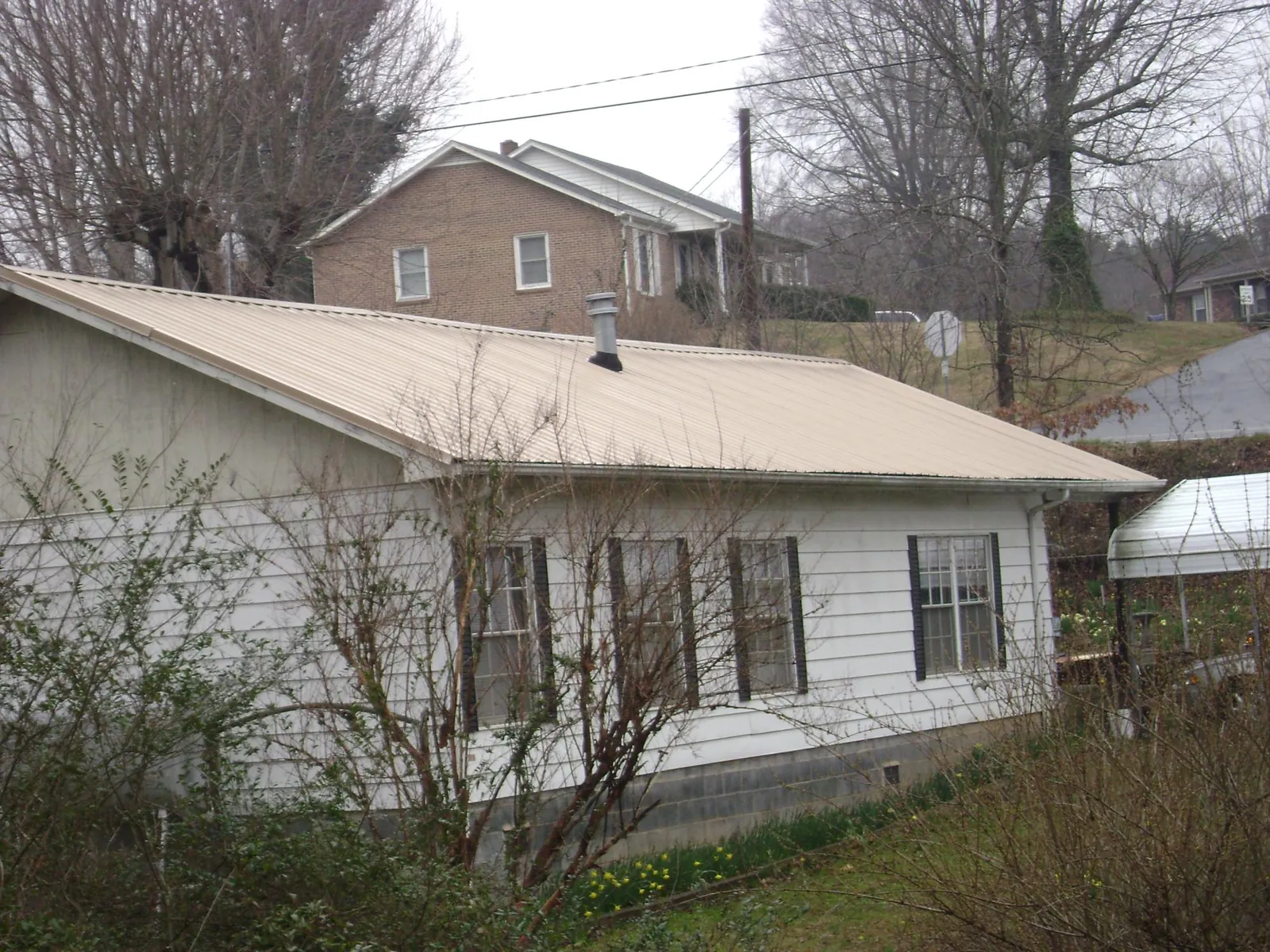 Tan metal roof on a white sided house set into a hillside — Commercial Roofing by Roofing Brothers in Southfield